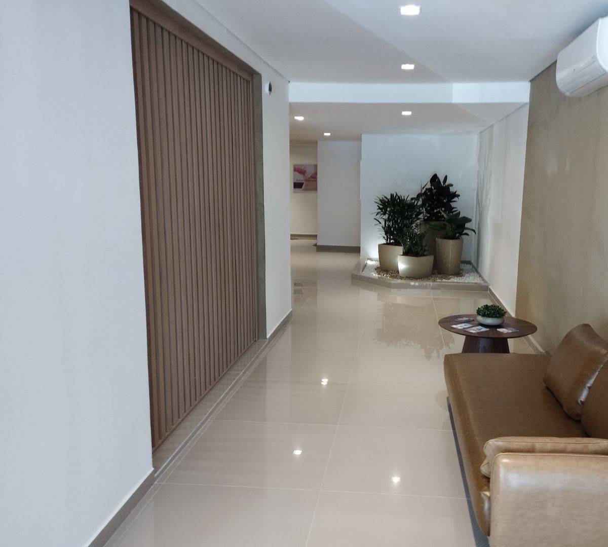 Corredor da clínica com sofá de couro, plantas e piso claro